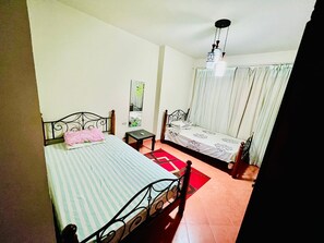 Un dormitorio con dos camas, una mesita, una lámpara colgante y una ventana con cortinas.