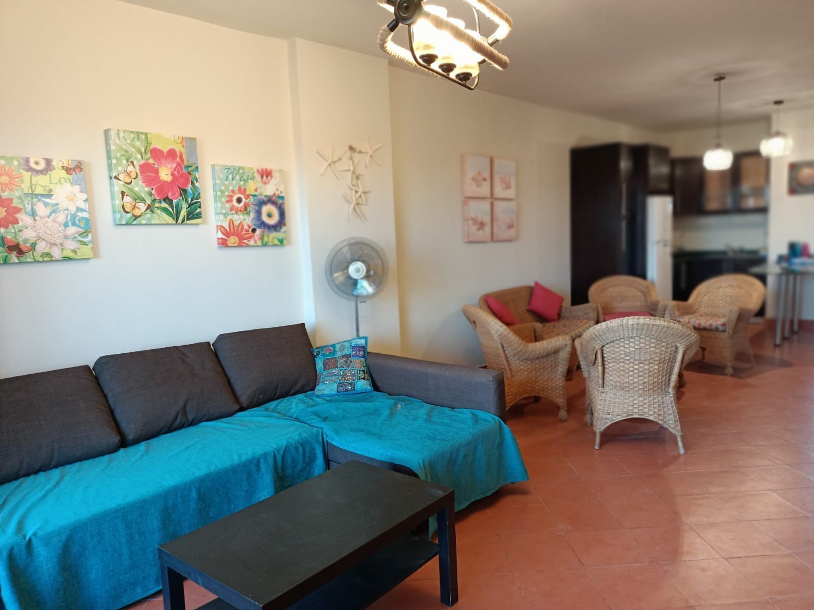 Ein Wohnzimmer mit einer Couch, Sesseln, einem Ventilator und Kunstwerken an den Wänden.