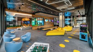 Un espai interior modern amb zones d'estar, una taula de futbolí i una màquina recreativa.
