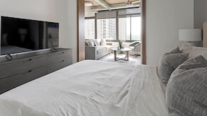 Ein Hotelzimmer mit Bett, Fernseher, Schreibtisch und Blick auf die Stadt durch große Fenster.