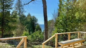 Une terrasse en bois, dotée de deux bancs et d’une rambarde, entourée d’arbres et offrant une vue sur une étendue d’eau.