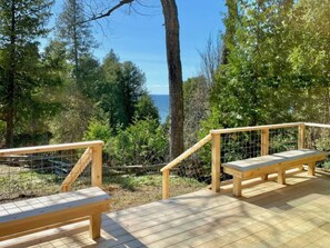 A wooden deck with two benches and a railing, surrounded by trees and overlooking a body of water.