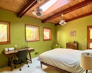 A bedroom with a bed, desk, chair, and two windows. - Goathaus | Iconic A-Frame with Bay Views (Sister Bay)