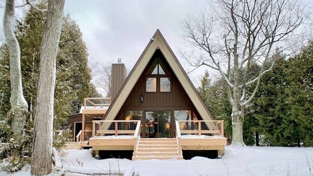 Une cabane dotée d’un toit triangulaire, d’une terrasse en bois et d’un escalier menant à l’entrée.