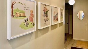 Un couloir avec des illustrations encadrées accrochées au mur, une porte et un luminaire suspendu.