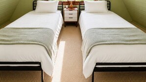 Une chambre avec deux lits, une fenêtre avec un cadre en bois et une petite table de chevet avec une lampe.