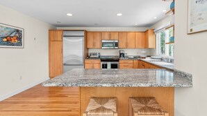 Une cuisine moderne dotée de plans de travail en granit, d’armoires en bois, d’appareils électroménagers en acier inoxydable et d’un grand îlot central avec des tabourets de bar.
