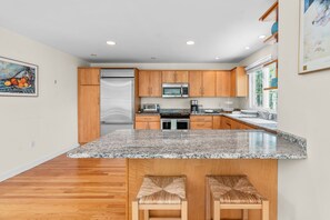 A modern kitchen with granite countertops, wooden cabinets, stainless steel appliances, and a large island with bar stools.