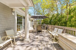 Une terrasse extérieure couverte, avec une table et des chaises, un grand parasol et une vue sur les arbres.