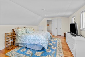 A bedroom with a bed, a TV, a dresser, a bookshelf, and a door leading to another room.