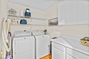 A laundry area with two front-loading washers, a dryer, shelves with laundry supplies, and a framed picture on the wall.