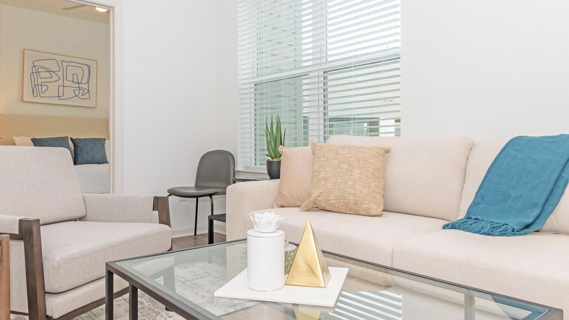 Un salon moderne avec un canapé, des fauteuils, une table basse en verre et une plante en pot.