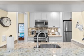 A kitchen with white cabinets, a stainless steel microwave, a stove, a refrigerator, and a wall clock.
