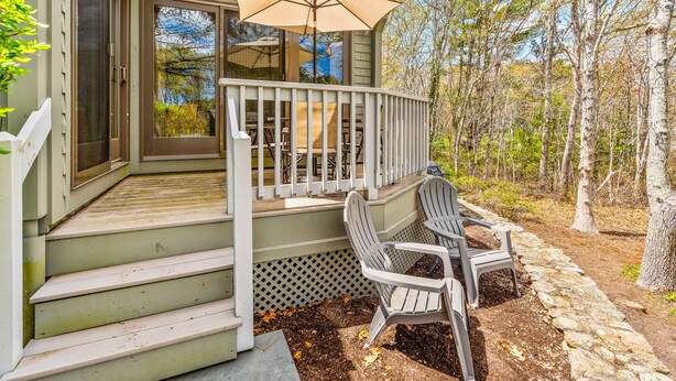 Een veranda met een witte balustrade, een bankje en een tafel onder een parasol.