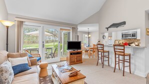 Een woonkamer met een televisie, bank en een eethoek met stoelen.