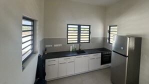 A kitchen with white cabinets, a black countertop, a stainless steel refrigerator, and two windows with blinds. - Casa Trankilo | Rest & beaches near Cas Abao (Bisento)