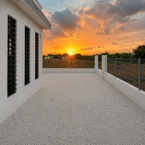 Eine Dachterrasse mit Blick auf den Sonnenuntergang, ein weißes Gebäude mit vergitterten Fenstern und einem Kiesboden.