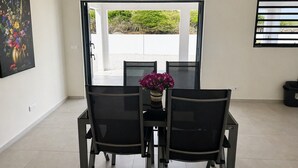 A dining area with a table and chairs, a vase with flowers, and a view through a glass door. - Casa Trankilo | Rest & beaches near Cas Abao (Bisento)