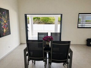 Un comedor con una mesa y sillas, un florero con flores y vistas a través de un ventanal.