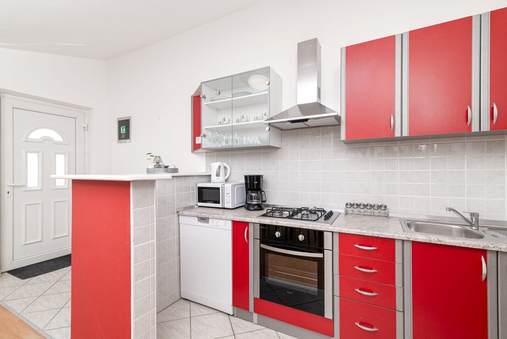 A kitchen with red cabinets, a white countertop, a microwave, a coffee maker, a gas stove, and a dishwasher.