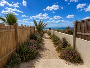 Un sentier bordé de plantes et une clôture en bois qui mènent à une plage.