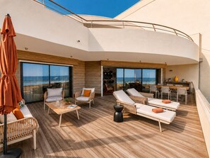 Une terrasse ensoleillée avec des chaises longues, une table et un coin repas offrant une vue sur la mer.