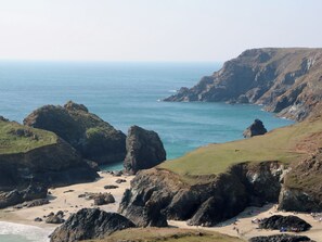 A coastal landscape with rocky cliffs, a sandy beach, and the ocean. - 14 Bosvigo (Helston)