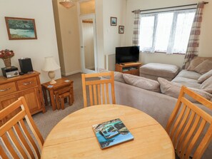 A cozy living room with a sofa, a TV stand, a dining table, and a chair. - 14 Bosvigo (Helston)