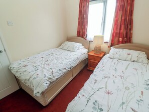 Ein Doppelbett mit floraler Bettwäsche, ein Nachttisch mit Lampe und ein Fenster mit Vorhängen.