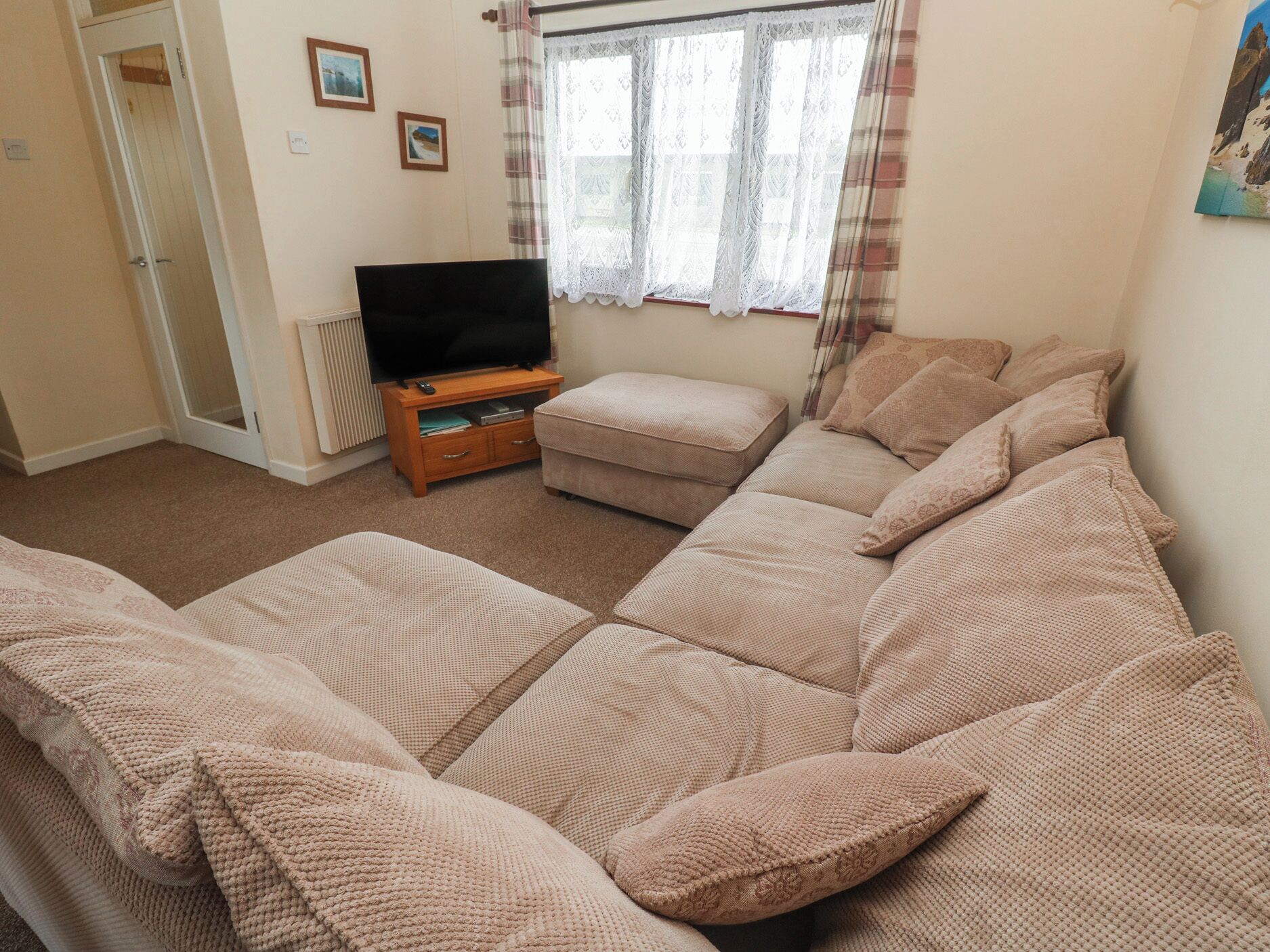 A living room with a sofa, a television on a stand, a window with curtains, and a door.