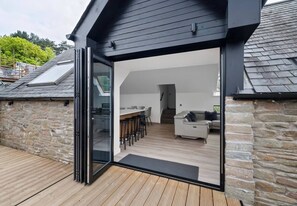 A modern house with a stone exterior, a wooden deck, and a glass door leading to an interior with a dining area and a living room. - Corn Flour Lodge, Pitkerro Mill (Dundee)