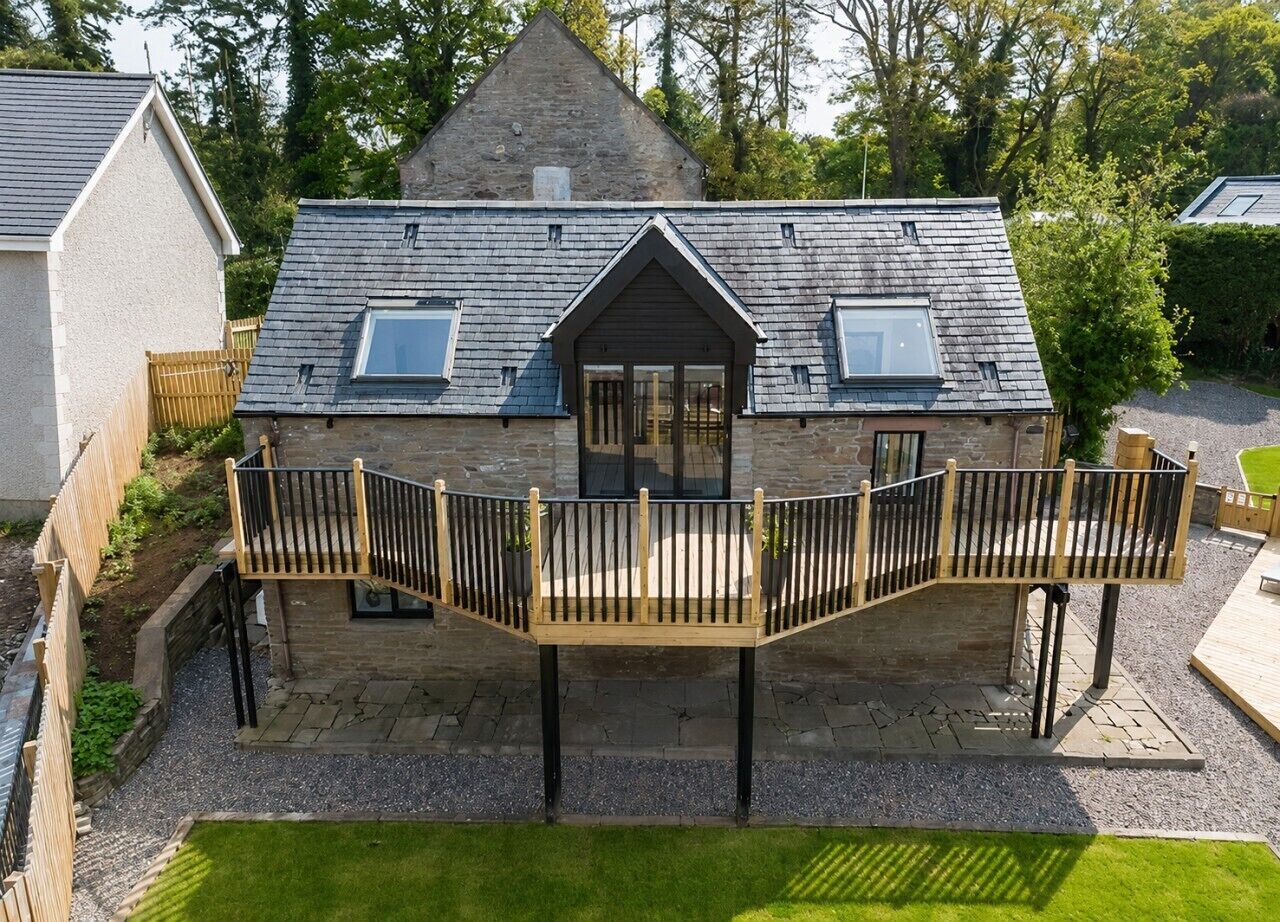 A two-story house with a balcony, stone walls, and a wooden deck.