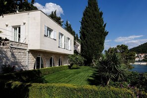 Ein modernes Gebäude mit Natursteinfassade, zahlreichen Fenstern mit Rollläden und einem gepflegten Rasen mit verschiedenen Pflanzen.