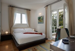 Ein Schlafzimmer mit Bett, Nachttischen, einem Fenster mit Vorhängen, einem Bild an der Wand und Blick nach draußen.
