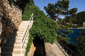 Eine steile Steintreppe führt zu einer Küstenlandschaft mit Blick auf das Meer und viel Grün.