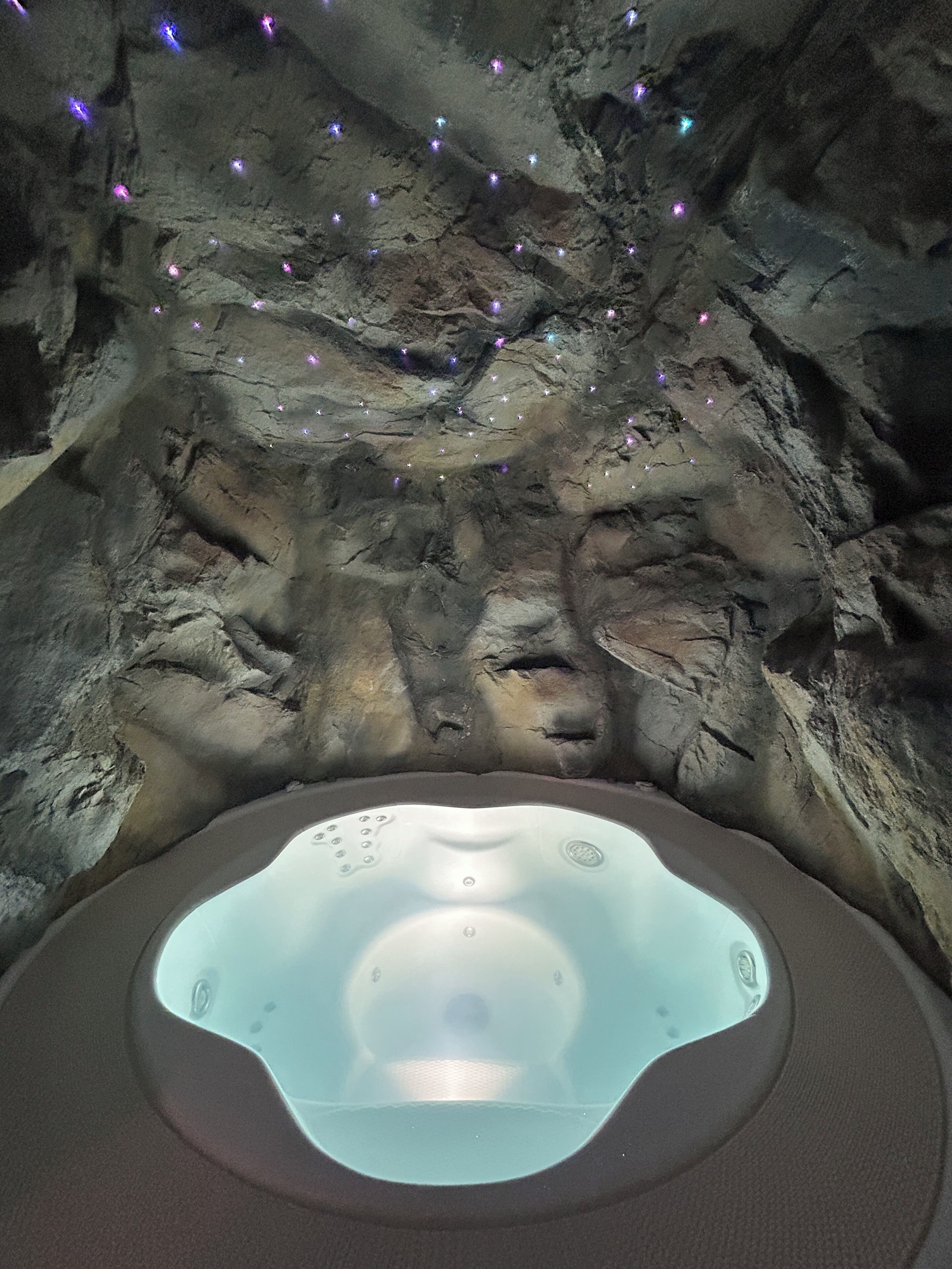 A hot tub in a cave-like setting with rock formations and small lights.