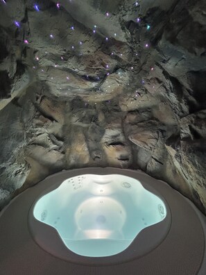 Un jacuzzi en un entorno similar a una cueva, con formaciones rocosas y pequeñas luces.