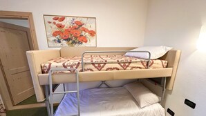 A bunk bed with a patterned bedspread, a white pillow, and a painting of red flowers on the wall. - Hotel Alpe Bellaria (Candriai)
