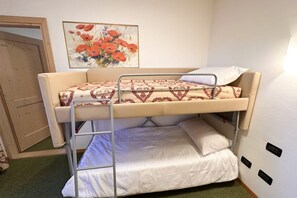 Una cama litera con una colcha estampada, un almohadón blanco y un cuadro de flores rojas en la pared.