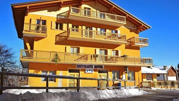 A multi-story hotel with balconies, a sign indicating it's a restaurant hotel, and a clear blue sky. - Hotel Alpe Bellaria (Candriai)