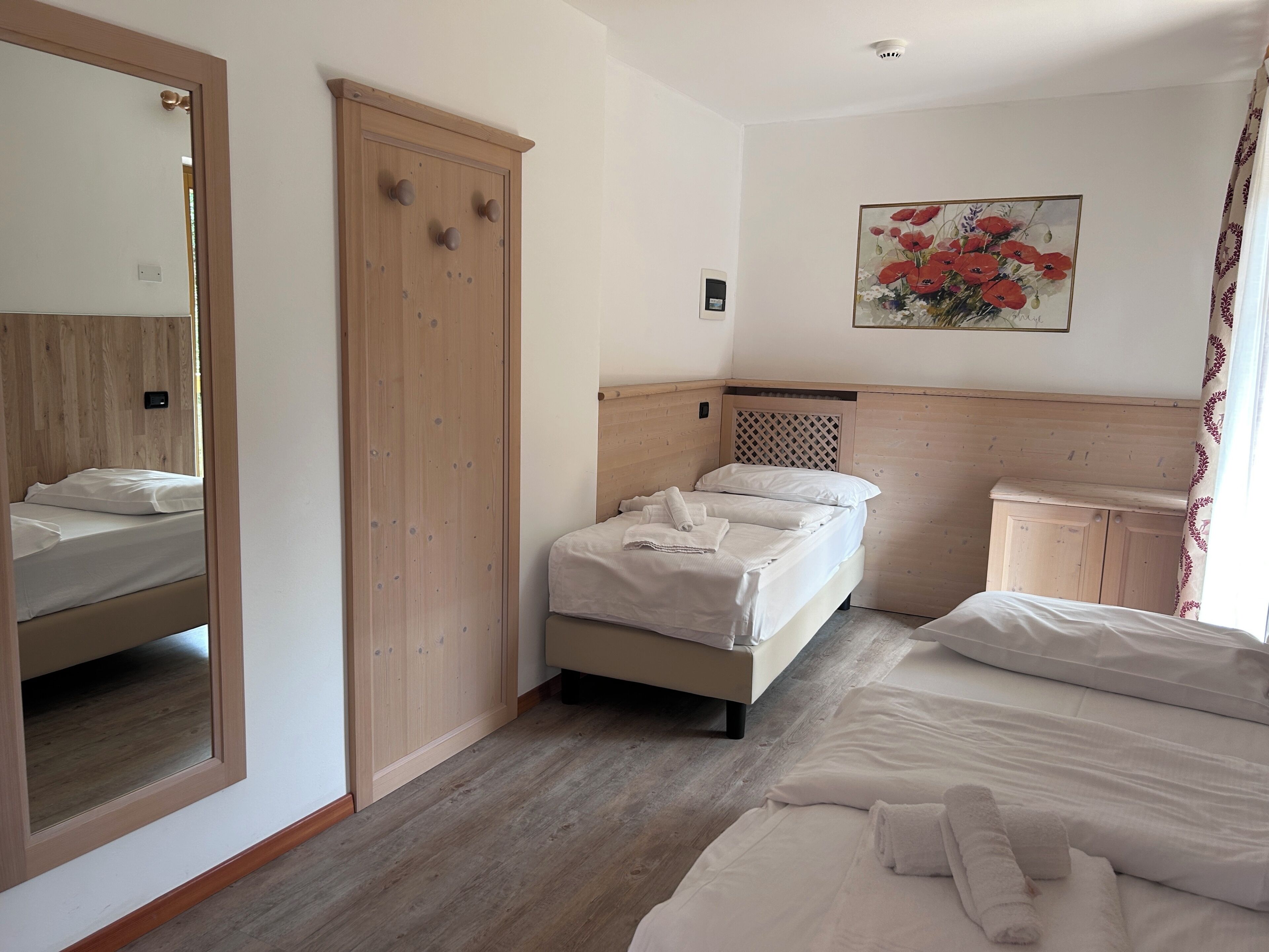 A bedroom with a bed, a wardrobe, a mirror, and a painting on the wall.