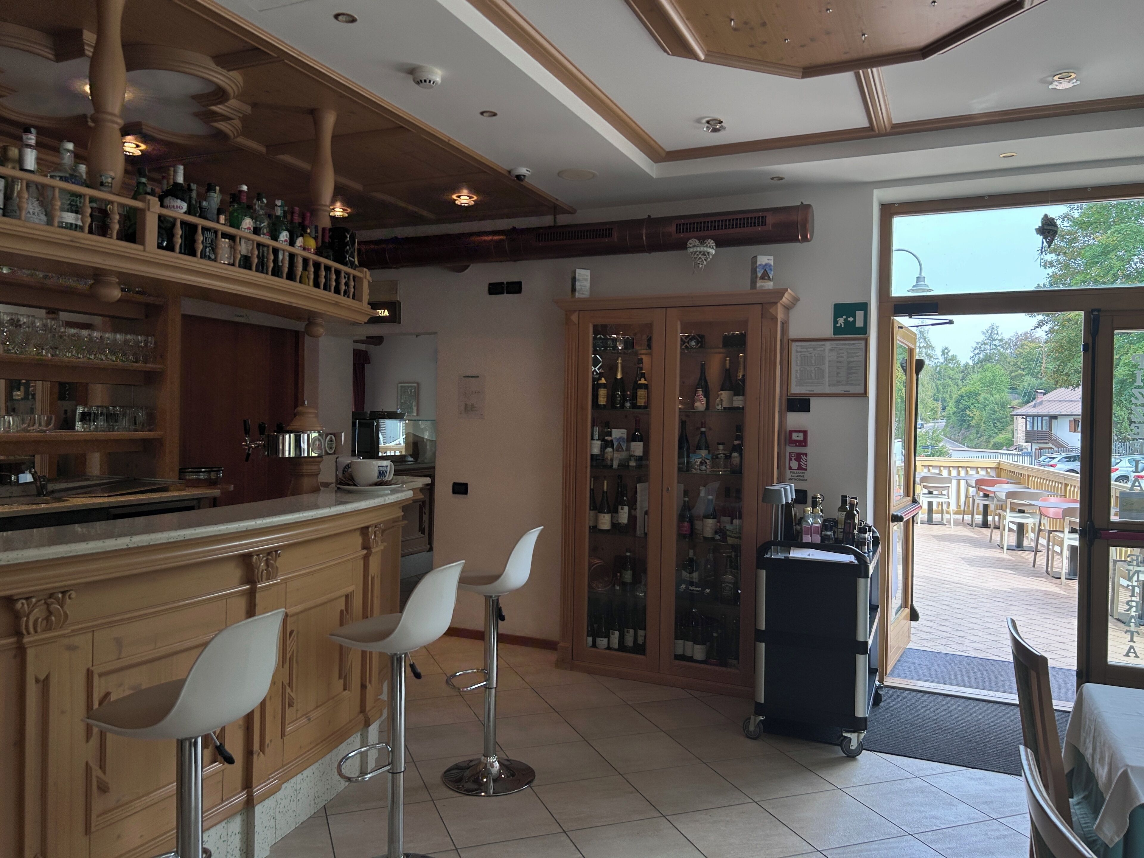 A bar area with stools, shelves of bottles, and a view of the outside.