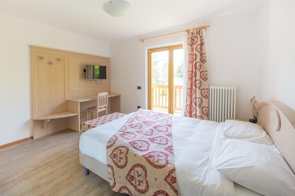 A bedroom with a bed, a desk, a chair, a television, and a window with curtains.