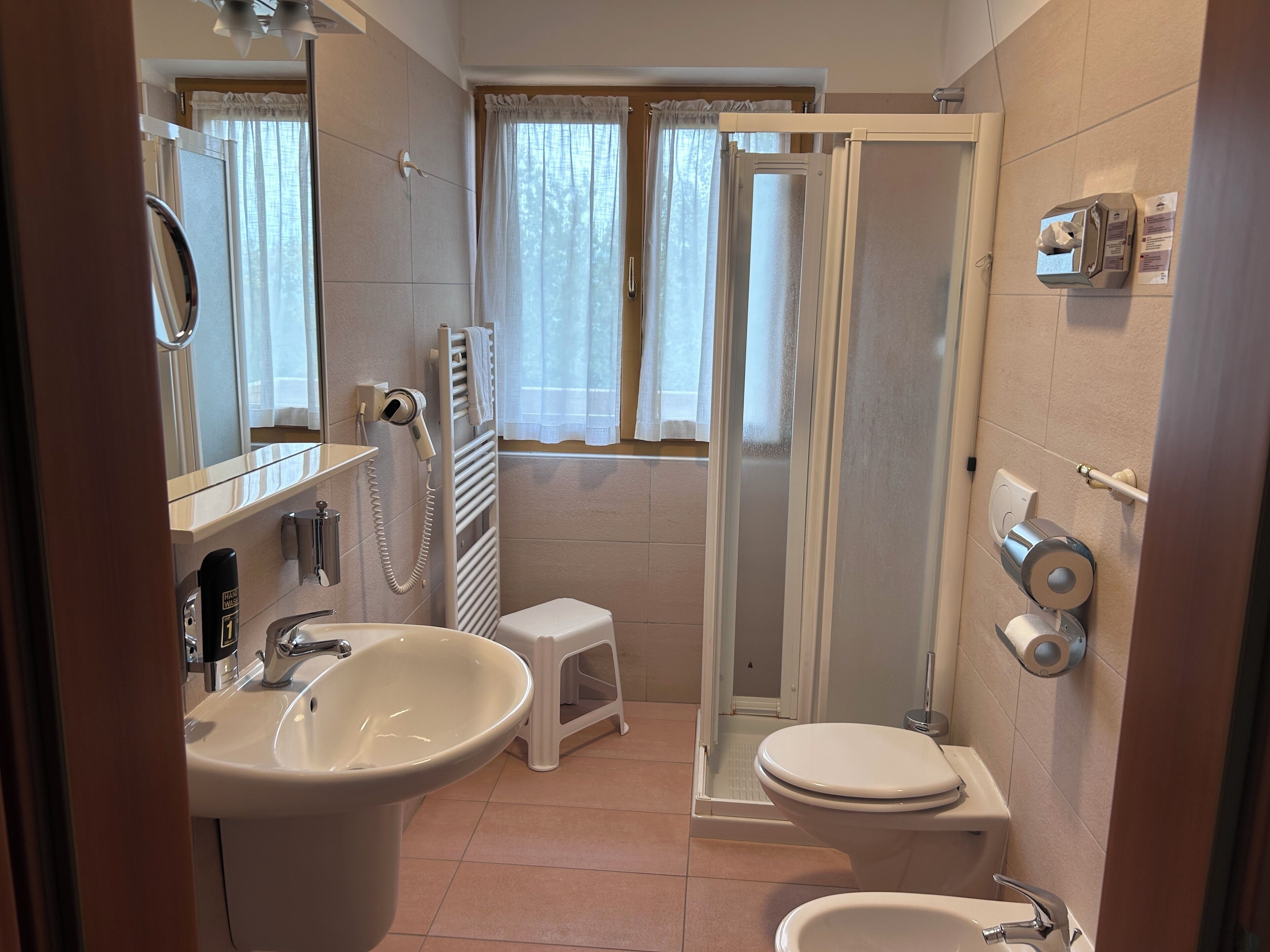 A bathroom with a sink, toilet, shower, and a small stool.