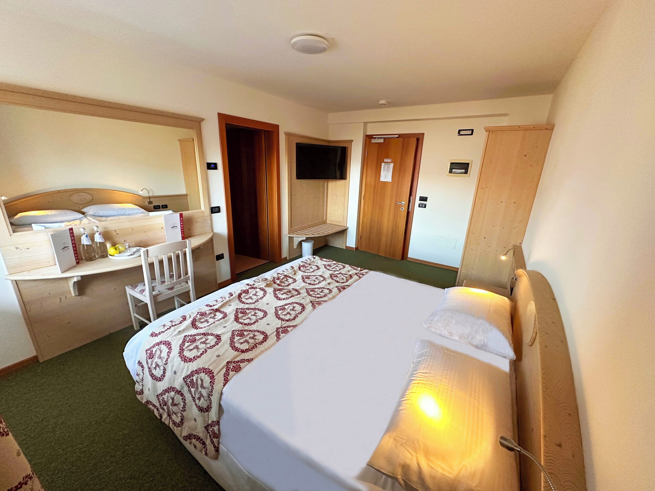 A hotel room with a bed, a desk, a chair, a television, and a wardrobe.