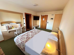 A hotel room with a bed, a desk, a chair, a television, and a wardrobe.