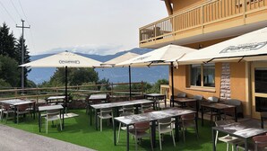 An outdoor seating area with tables and chairs, umbrellas, and a view of mountains. - Hotel Alpe Bellaria (Candriai)