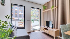 Un saló modern amb un sofà, un televisor sobre una consola de fusta i un balcó amb plantes.