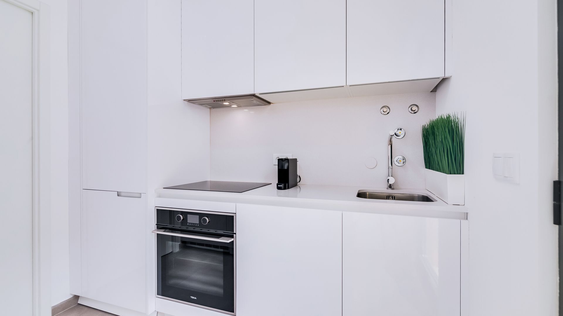 Uma cozinha moderna com armários brancos, forno embutido, máquina de café e pia com torneira.