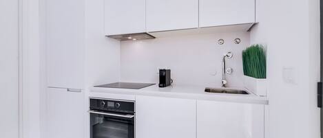 Uma cozinha moderna com armários brancos, forno embutido, máquina de café e pia com torneira.